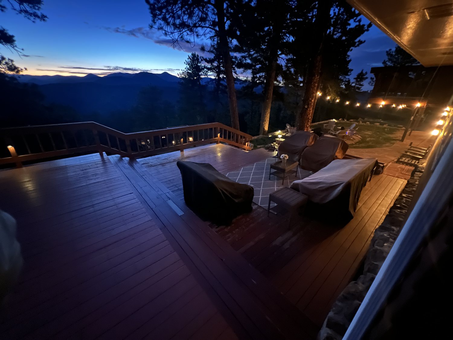 Deck seating and string lights after sunset with the mountains beyond