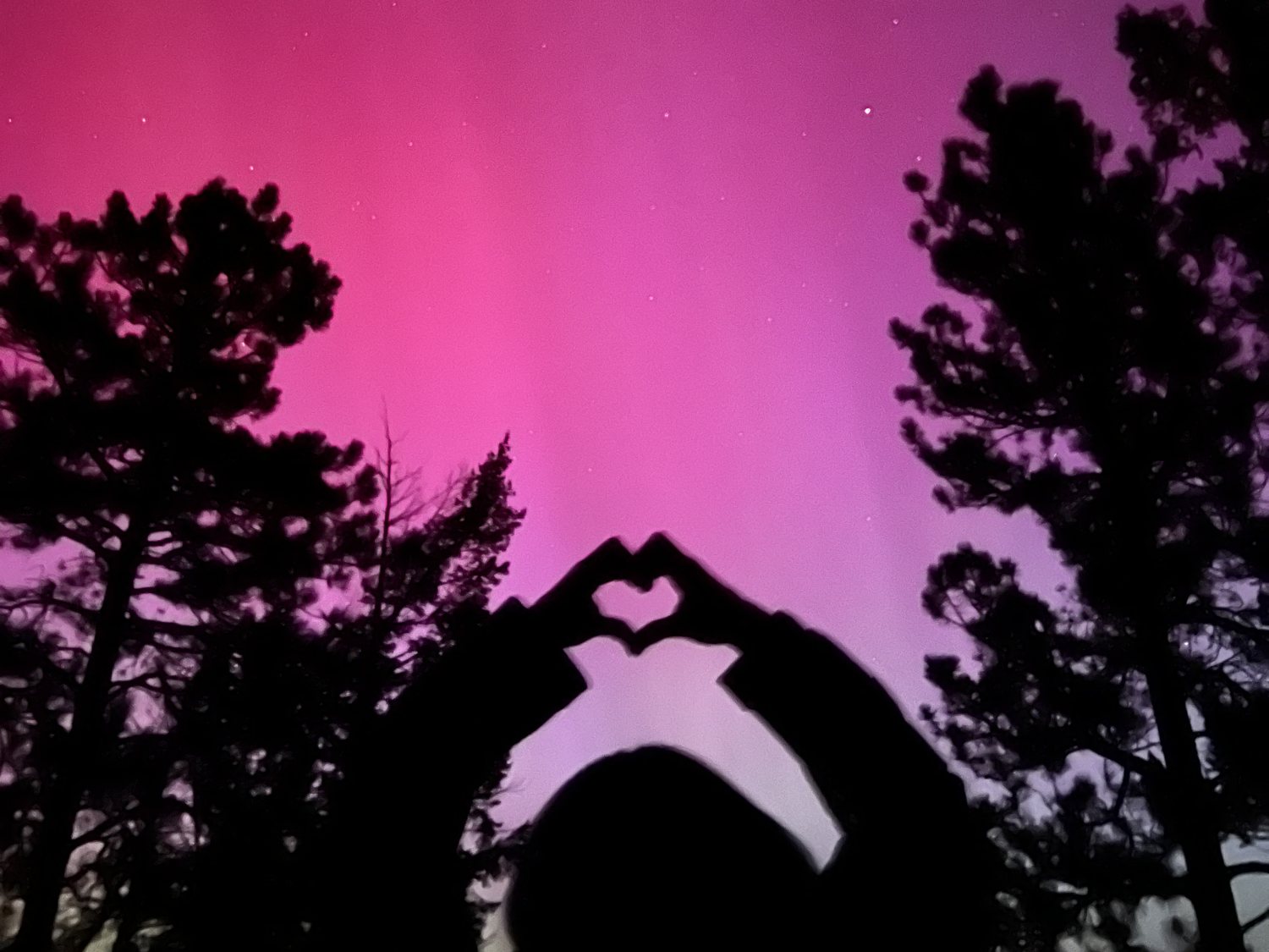 Two people silhouetted against a magenta aurora, hands raised in the shape of a heart