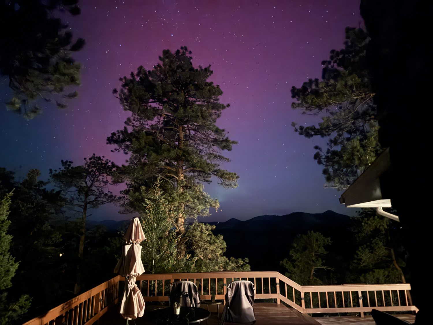 The deck railing and mountains beneath a violet and magenta aurora